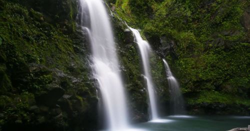 A serene waterfall cascading over moss-covered rocks into a tranquil pool below, surrounded by lush greenery.