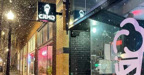 A snowy street scene featuring a brightly lit ice cream shop with a neon sign reading "CRMD."