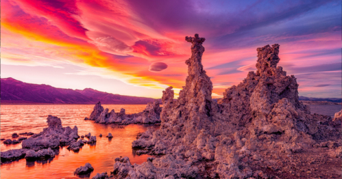 Colorful sunset over unique rock formations by a lake, with vibrant clouds reflecting in the water.