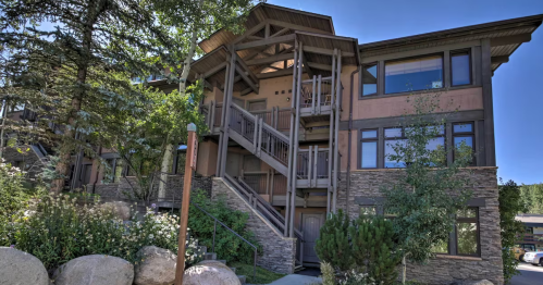 A multi-story building with wooden accents, surrounded by trees and rocks, under a clear blue sky.