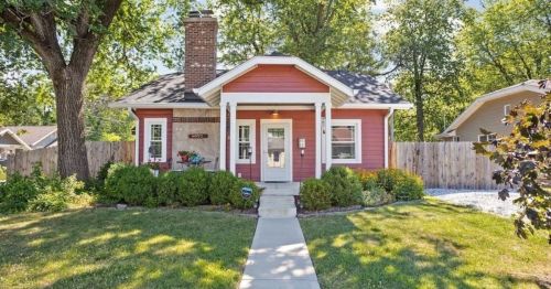 Charming red house with a front porch, surrounded by greenery and a well-maintained garden.