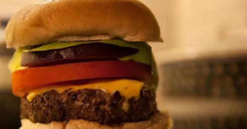 A close-up of a juicy cheeseburger with layers of lettuce, tomato, onion, and a soft bun.