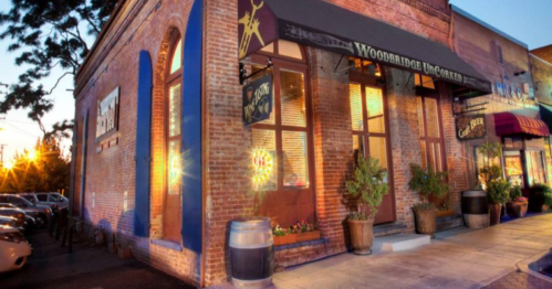 Exterior of a brick restaurant with large windows, planters, and a warm sunset glow.