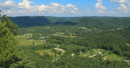 A panoramic view of lush green hills and valleys under a blue sky with fluffy clouds.
