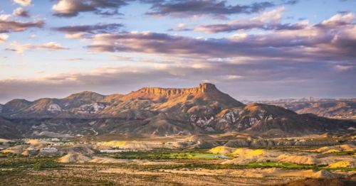 A scenic view of a mountainous landscape under a cloudy sky, with rugged terrain and soft sunlight illuminating the peaks.