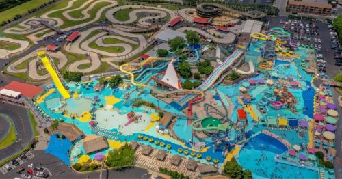 Aerial view of a vibrant water park with slides, pools, and go-kart tracks, surrounded by greenery and parking areas.