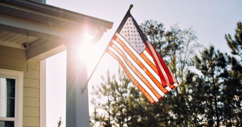 An American flag waves gently in the sunlight, with trees in the background.