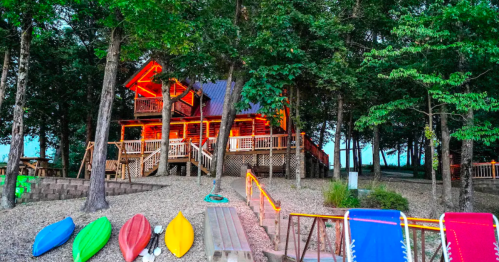 A cozy cabin surrounded by trees, with colorful kayaks in front and warm lights illuminating the structure at dusk.