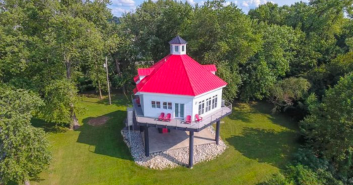 Aerial view of a unique round house with a red roof, surrounded by trees and a grassy area.