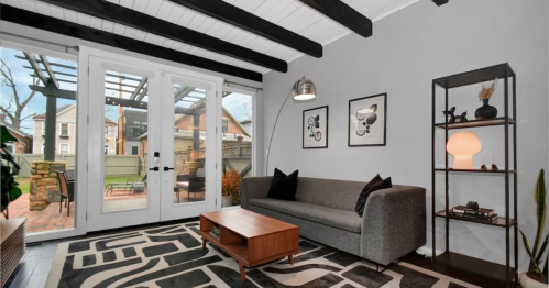 Modern living room with a gray sofa, wooden coffee table, and large windows opening to a patio. Stylish decor and plants.