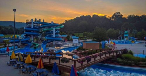A water park at sunset featuring colorful slides, pools, and lounge chairs under a scenic sky.