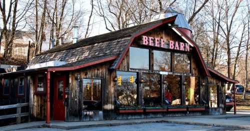 A rustic restaurant called "Beef Barn" with large windows, wooden exterior, and a sloped roof, surrounded by trees.