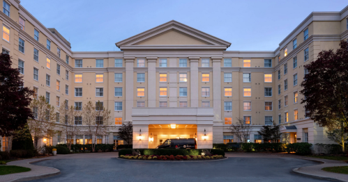 A modern hotel building with a grand entrance, illuminated windows, and landscaped surroundings at dusk.