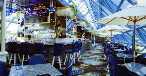 Bright, modern restaurant interior with blue decor, an oyster bar, and large windows letting in natural light.