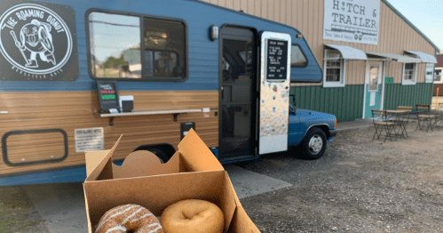 A food truck named "The Roaming Donut" with a box of two donuts in the foreground, set in a casual outdoor dining area.