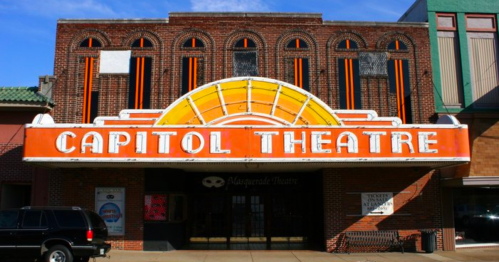 Exterior of the Capitol Theatre featuring a bright orange marquee and brick facade under a blue sky.