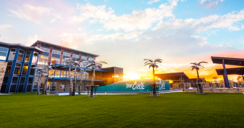 A modern building with palm trees at sunset, featuring a sign that reads "The Cove" against a colorful sky.