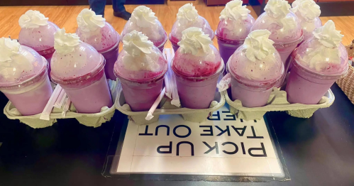 A tray of purple milkshakes topped with whipped cream and raspberry sauce, ready for pickup.