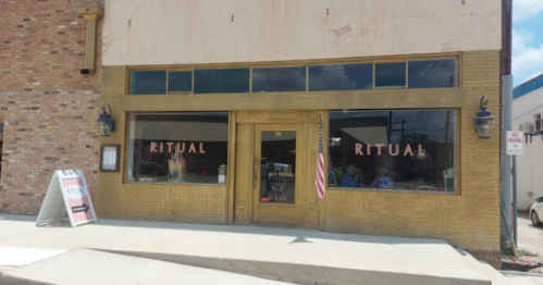 Exterior of a store named "Ritual," featuring large windows and a sign, with an American flag displayed.