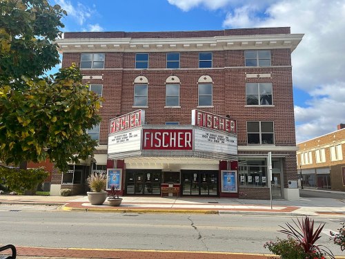 Historic Fischer Theater building with a marquee, surrounded by trees and a clear blue sky.