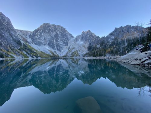 A serene mountain lake reflecting rugged peaks and clear blue skies, surrounded by autumn foliage.