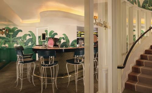 A stylish bar area with green palm leaf wallpaper, a circular counter, and elegant seating.