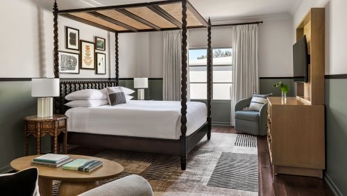 A stylish hotel room featuring a four-poster bed, modern decor, and a cozy seating area with natural light.