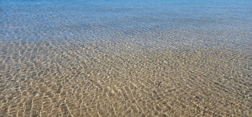 Clear blue water gently rippling over a sandy ocean floor, creating a serene and tranquil scene.