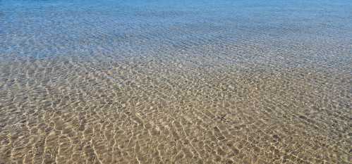 Clear blue water gently rippling over a sandy ocean floor, creating a serene and tranquil scene.