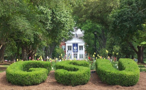 A landscaped area with trimmed bushes forming "GSU," in front of a building surrounded by trees and flowers.