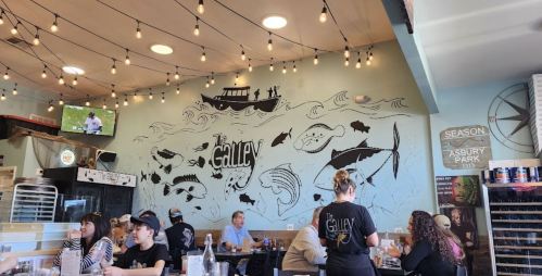 A bustling restaurant interior with a mural of fish and a boat, string lights overhead, and diners enjoying their meals.
