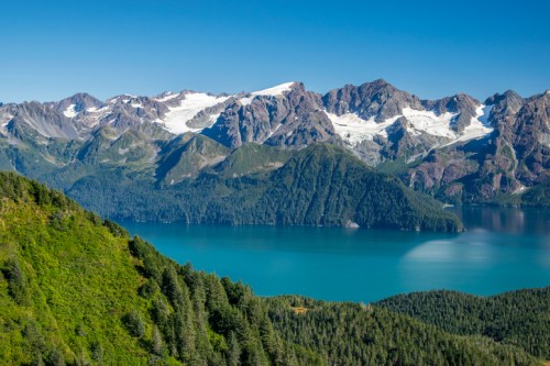 A stunning landscape featuring mountains, a glacial lake, and lush greenery under a clear blue sky.