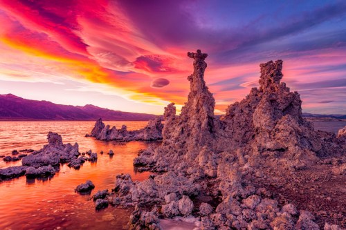 Colorful sunset over a lake with unique rock formations and vibrant clouds reflecting on the water's surface.