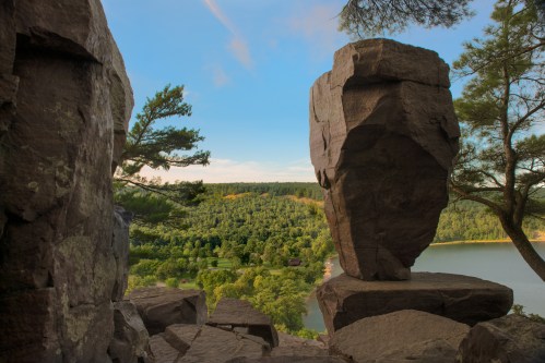 A scenic view of a lake surrounded by lush greenery, framed by large rock formations under a clear blue sky.