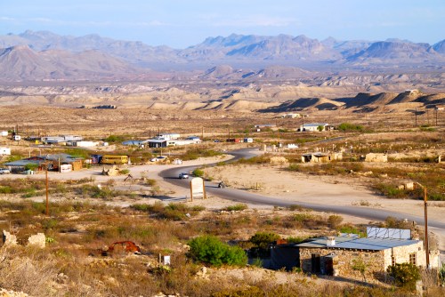 A vast desert landscape with mountains in the background, scattered buildings, and a winding road.