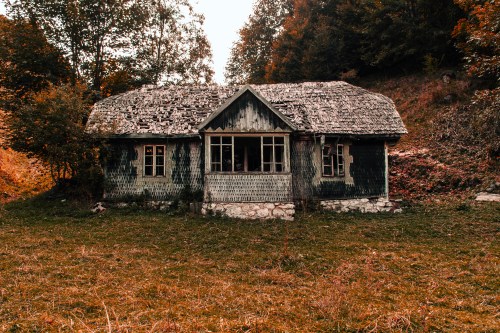 An old, weathered house with a thatched roof, surrounded by trees and grass in an autumn landscape.