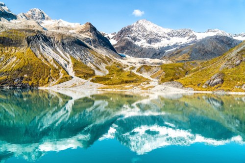 A serene mountain landscape with a turquoise lake reflecting snow-capped peaks and clear blue skies.