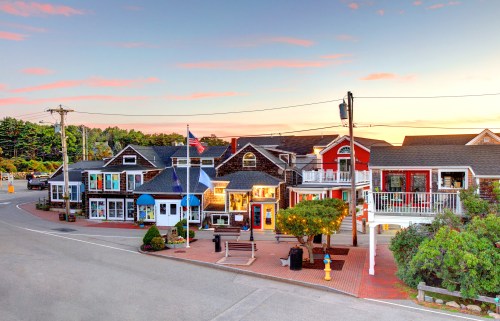 Charming small town street with colorful buildings, shops, and a sunset sky in the background.