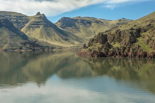 Serene landscape featuring mountains reflected in calm water under a cloudy sky.