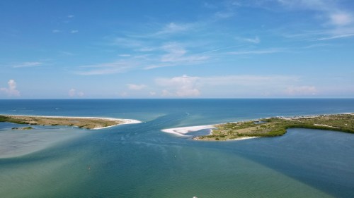 Aerial view of a serene coastal landscape with blue waters, sandy shores, and lush greenery under a clear sky.