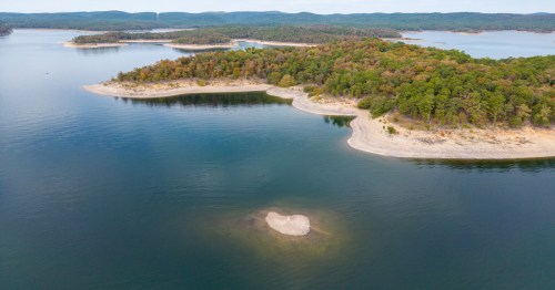Aerial view of a serene lake with islands and lush green trees along the shoreline, reflecting calm waters.