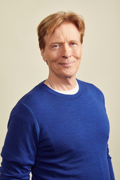A smiling man with light brown hair wearing a blue sweater against a neutral background.
