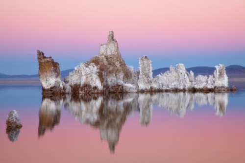 A serene landscape featuring unique rock formations reflected in calm water, with a pastel-colored sky at sunset.