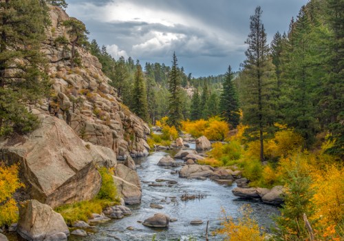 A serene river flows through a rocky landscape, surrounded by trees and vibrant autumn foliage under a cloudy sky.