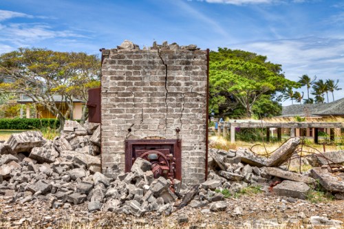 A crumbling brick structure surrounded by debris and overgrown vegetation under a blue sky.