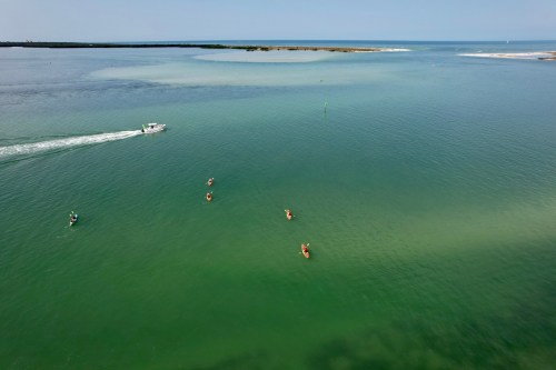 Aerial view of a calm green sea with people kayaking and a boat in the distance.