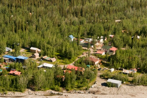 Aerial view of a small village surrounded by dense green trees and a river, featuring various houses with colorful roofs.