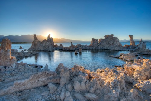 Sunset over a serene lake with unique rock formations and calm waters reflecting the warm colors of the sky.