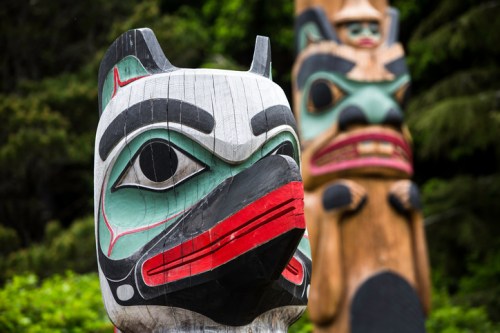 Two colorful totem poles with intricate carvings, set against a lush green background.