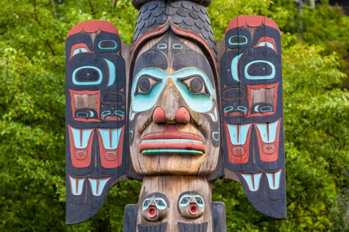A colorful totem pole featuring intricate carvings of faces and animal motifs against a green background.